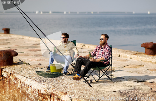 Image of happy friends fishing and drinking beer on pier