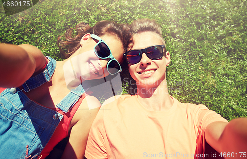 Image of happy teenage couple taking selfie on summer grass
