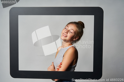 Image of Lovely girl standing behind digital tablet frame smiling enjoying with closed eyes