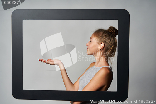 Image of Profile of teen girl standing behind digital tablet frame and showing blank copy space on her palm