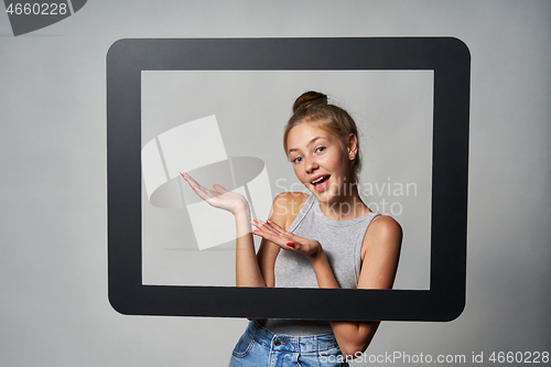 Image of Happy excited teen girl looking through digital tablet frame and showing directing to blank copy space