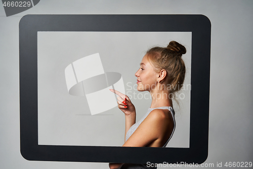 Image of Profile of girl standing behind digital tablet frame and pointing a finger at blank copy space