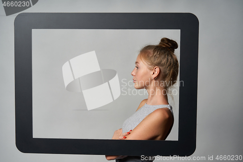 Image of Profile of girl standing behind digital tablet frame and looking forward at blank copy space