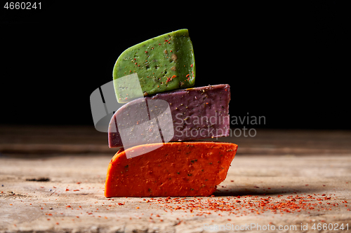 Image of Three different cheeses on rough wooden planks: lavender, paprika and pesto cheeses