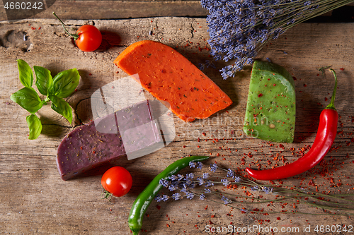 Image of Three different cheeses on rough wooden planks: lavender, paprika and pesto cheeses