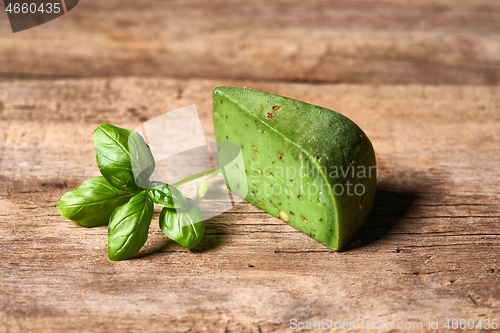 Image of A piece of gourmet basil cheese with twig of basil on rough wooden planks