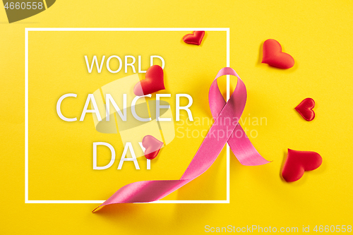 Image of the text world cancer day and a pink ribbon on a table background