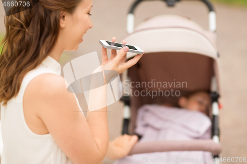 Image of happy mother with smartphone and stroller at park