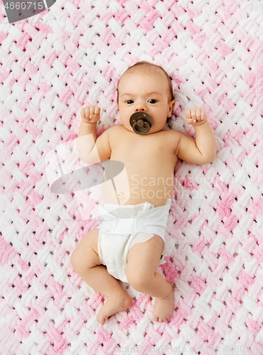 Image of baby girl in diaper lying with pacifier on blanket