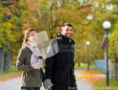 Image of couple with tumbler walking along autumn park