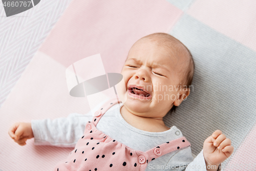 Image of crying baby girl lying on knitted blanket