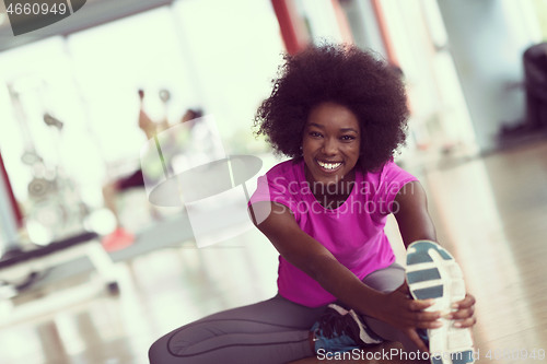 Image of woman in a gym stretching and warming up man in background worki