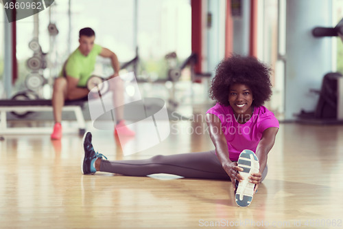 Image of woman in a gym stretching and warming up man in background worki