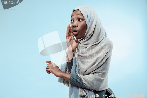 Image of The young african woman whispering a secret behind her hand over blue background