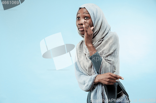 Image of The young african woman whispering a secret behind her hand over blue background