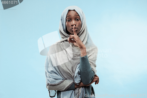 Image of The young african woman whispering a secret behind her hand over blue background