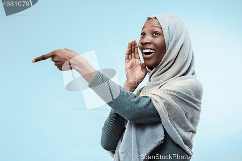 Image of The young african woman whispering a secret behind her hand over blue background