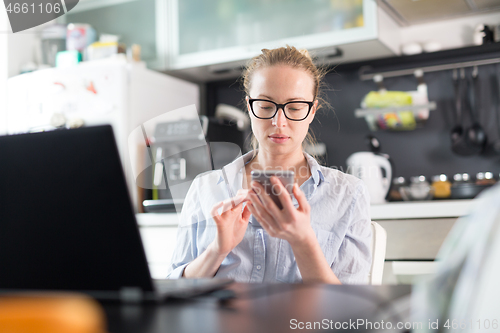 Image of Stay at home and social distancing. Woman in her casual home clothing working remotly from kitchen dining table. Video chatting using social media with friend, family, business clients or partners