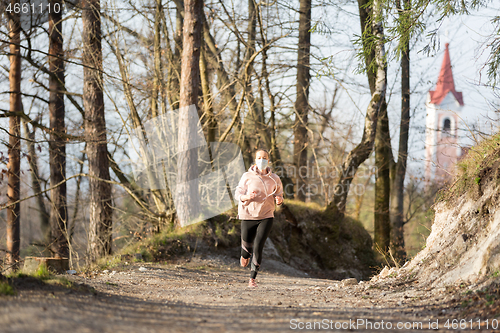 Image of Corona virus, or Covid-19, is spreading all over the world. Portrait of caucasian sporty woman wearing a medical protection face mask while running in nature.