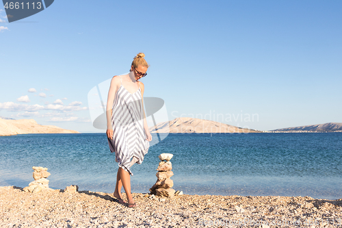 Image of Happy carefree woman enjoying late afternoon walk on white pabbled beach on Pag island, Croatia