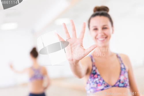 Image of Fit sporty active woman smiling, wearing fashion sportswear showing an open palm to the camera in yoga studio. Active urban lifestyle.