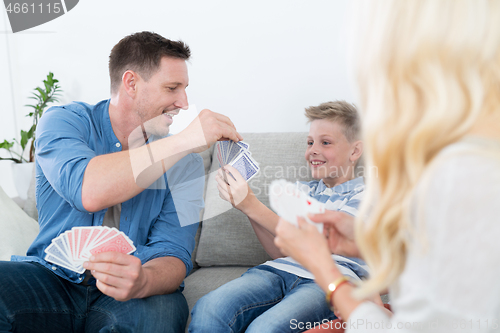 Image of Happy young family playing card game at home.