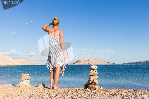 Image of Happy carefree woman enjoying late afternoon walk on white pabbled beach on Pag island, Croatia