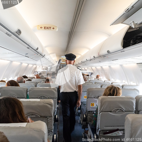 Image of Interior of commercial airplane with flight attandant serving passengers on seats during flight. Steward in uniform walking the aisle.square composition