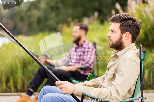 Image of male friends with fishing rods on lake