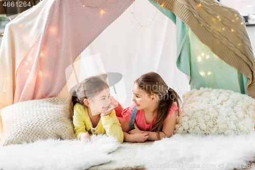 Image of happy girls lying in kids tent and talking at home