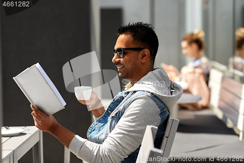 Image of man reading book and drinking coffee at city cafe