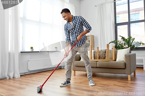 Image of man with broom cleaning floor at home