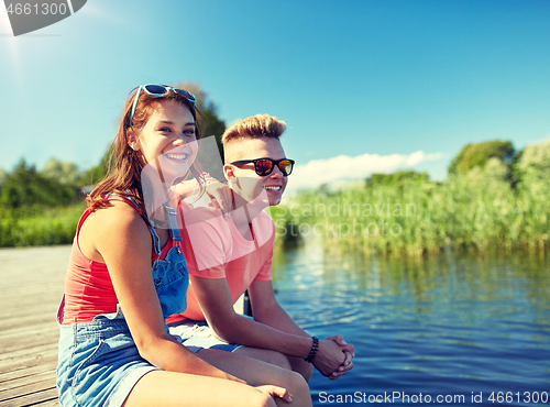 Image of happy teenage couple sitting on river berth