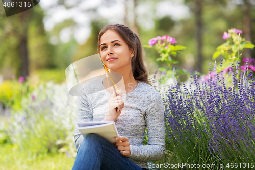 Image of young woman writing to notebook at summer garden