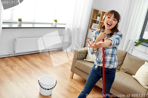 Image of asian woman or housewife with mop singing at home