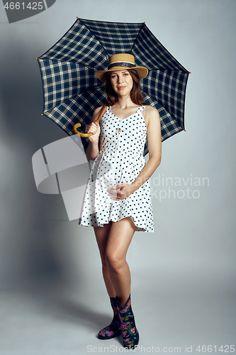 Image of Pregnant woman in country style summer dress and straw hat standing under umbrella
