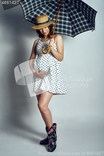 Image of Pregnant woman in country style summer dress and straw hat standing under umbrella