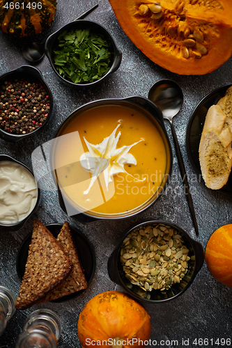 Image of Delicious pumpkin soup with cream, seeds, bread and fresh herbs 