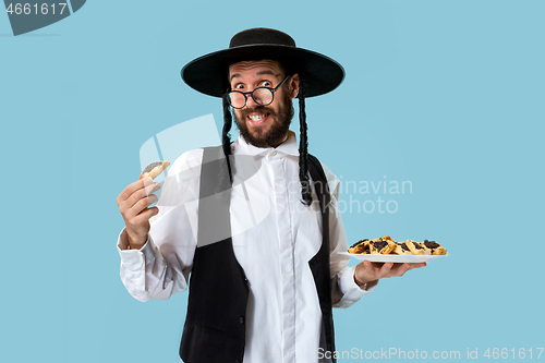 Image of The young orthodox Jewish man with black hat with Hamantaschen cookies for Jewish festival of Purim