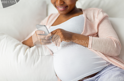 Image of pregnant woman with smartphone in bed at home