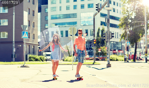 Image of teenage couple riding skateboards on city street