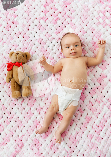 Image of baby girl in diaper lying with teddy on blanket