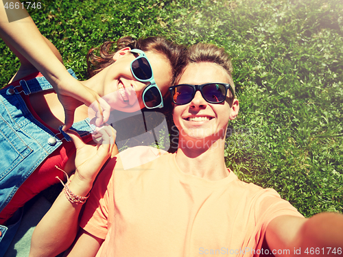 Image of happy teenage couple taking selfie on summer grass