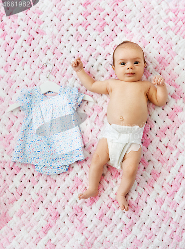 Image of baby girl in diaper lying with dress on blanket