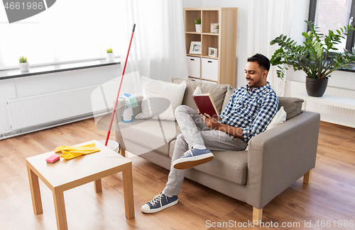 Image of man reading book and resting after home cleaning