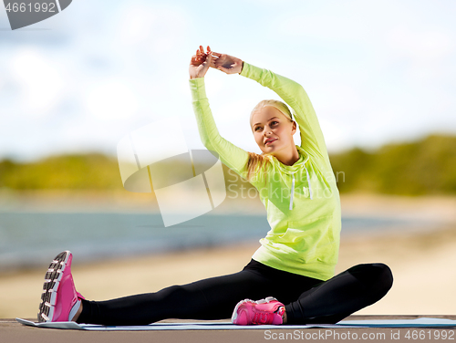 Image of woman stretching on exercise mat on beach