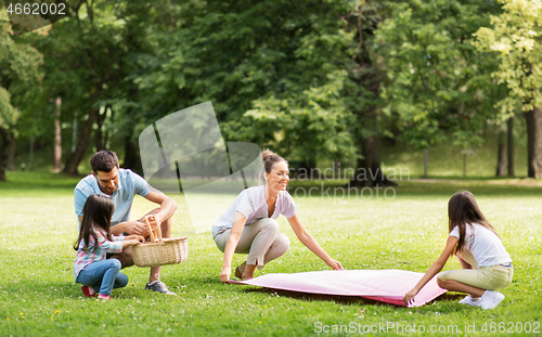 Image of family laying down picnic blanket in summer park