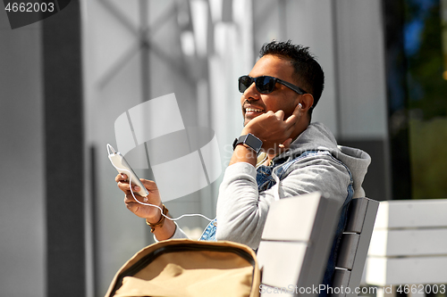 Image of man with earphones and smartphone on city street