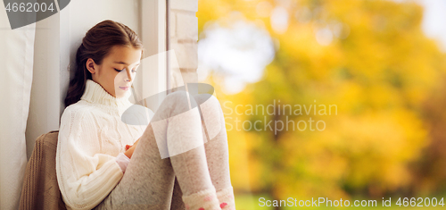 Image of sad girl sitting on sill at home window in autumn