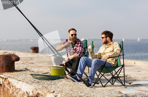 Image of male friends fishing and drinking beer on pier